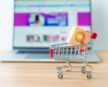 Miniaturowy wózek sklepowy z ikoną wyszukiwarki przed ekranem laptopa